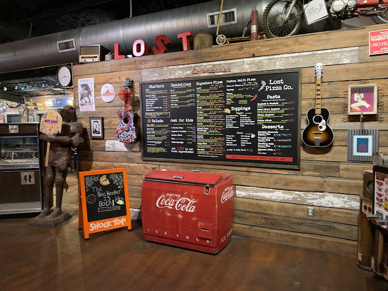 Vintage signs, guitars, and roadside finds on a Lost Pizza Co. wall